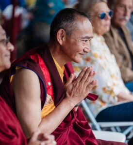 We see a Buddhist Monk in robes with folded hands and a smile. It shows the devotion of Dilyak Drupon Rinpoche towards fulfilling the aspirations of Karmapa Center 16 and kind presence to all.